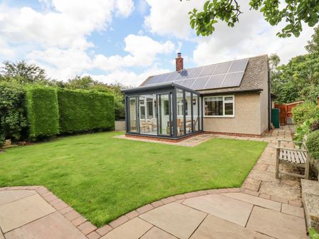 A house with solar panels and a conservatory surrounded by a lawn and paved walkways at Manor Cottage in Embleton
