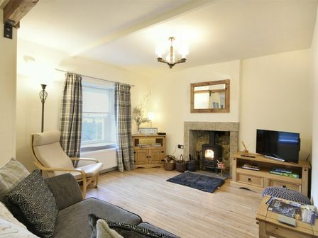 A living room with a wood stove fireplace a TV on a wooden stand and a chair at West End Cottage in Embleton