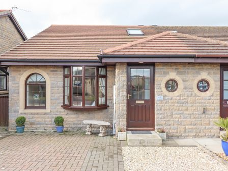 The front exterior of a stone house with a brown door, arched and circular windows, potted plants, and a stone bench at The Bolthole in Seahouses
