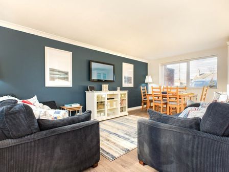 A living room with two dark sofas a white cabinet with a TV on the wall and a wooden dining table with chairs at Stones Throw in Beadnell