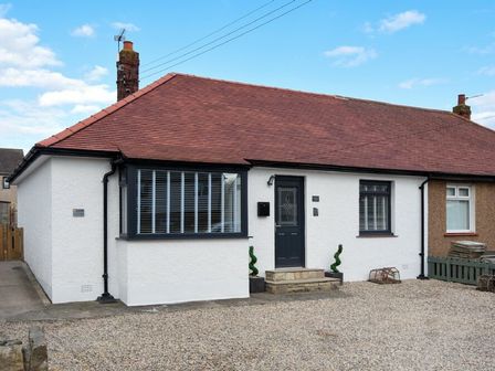 A white bungalow with a red roof black door and windows with blinds at Anchor Lodge in Seahouses