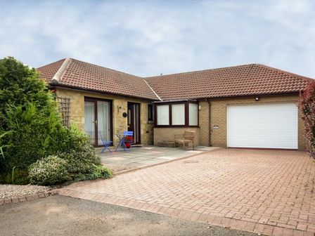 A driveway leading to a house with a tiled roof a garage door and outdoor seating at Summerfold in Warkworth