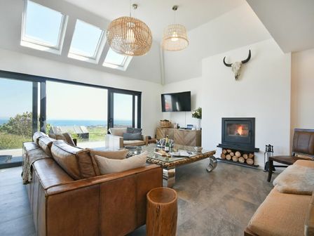 A living room with large windows overlooking a landscape and ocean with sofas a fireplace and a mounted skull at Waters Edge Beadnell Harbour Road in Beadnell