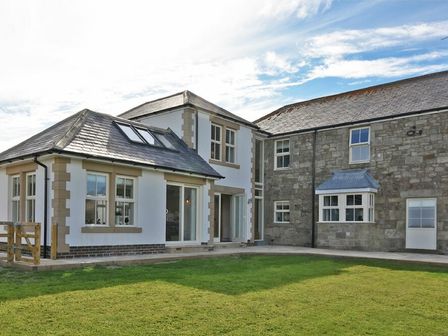 A house with white and stone walls and a grass lawn at South View nr Bamburgh in Seahouses
