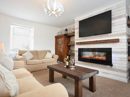 A living room with beige sofas a wooden coffee table a mounted tv and an electric fireplace at Rivershield in Warkworth