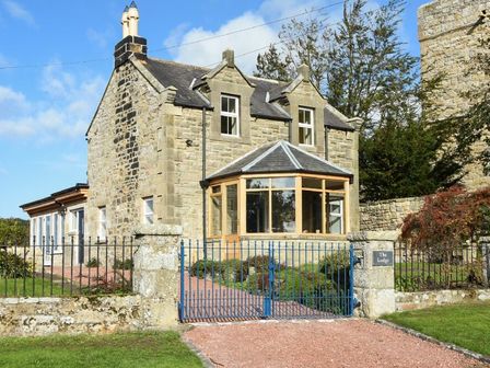 A stone house with a glass conservatory and blue gate at The Lodge Elsdon