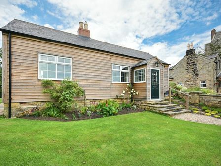 A wooden cottage with a small porch surrounded by a garden and lawn at Rose Cottage Elsdon