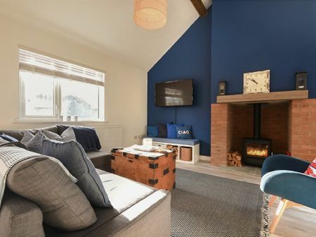 A living room with a gray sofa a wooden chest coffee table and a fireplace with a blue accent wall at Bowline Cottage in Beadnell