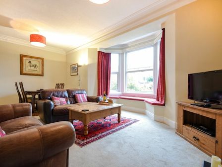 A living room with leather sofas a wooden coffee table a bay window with seating and a television on a wooden stand at Sunnybrae Alnmouth