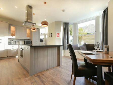 A kitchen with an island and dining table with black chairs near a bay window at Sandybrae in Alnmouth