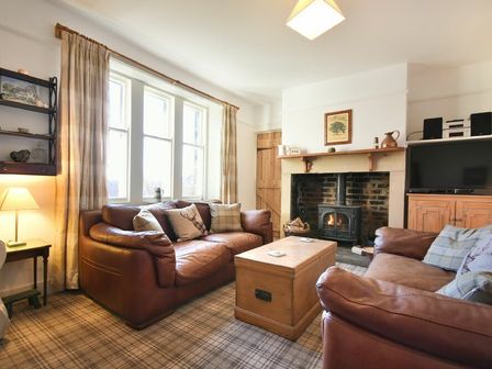 A living room with two brown leather sofas a wooden chest coffee table and a wood stove fireplace at Whistlewood in Bamburgh