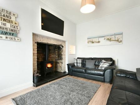 A living room with black leather sofas a wood burning stove and a wall mounted television at Hillcrest in Seahouses