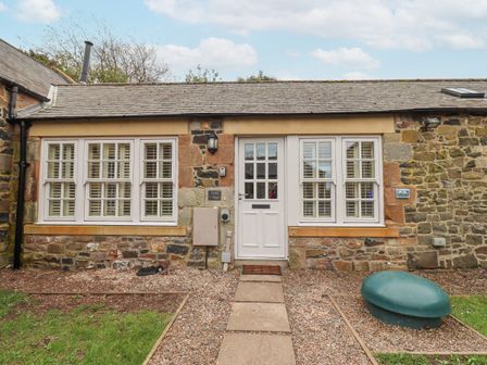 Front entrance of a stone cottage with white framed windows and a white door at Coral Cottage in Bamburgh
