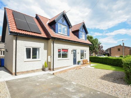 A detached house with a tiled roof and solar panels a bench outside and a gravel driveway at The Chevy in Seahouses
