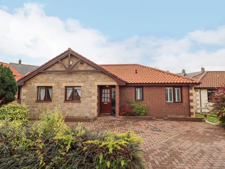 A single story house with brick and stone walls and a tiled roof with shrubs in front at Rokeby in Bamburgh