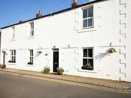 The exterior of a white house with multiple windows a black door and flower pots on the sidewalk at The Bakehouse in Seahouses