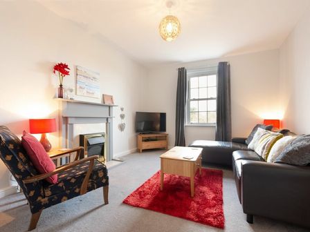 A living room with a fireplace a television a sofa an armchair and a red rug at Church View in Bamburgh