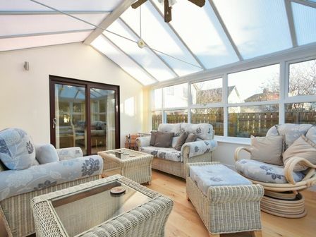 A sunroom with wicker furniture and large windows at Annstead House in Seahouses