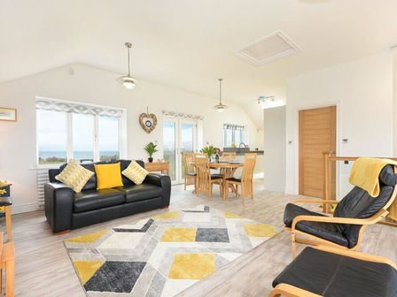 An open living and dining area with black leather sofa and wooden dining table at Viewpoint in Alnmouth