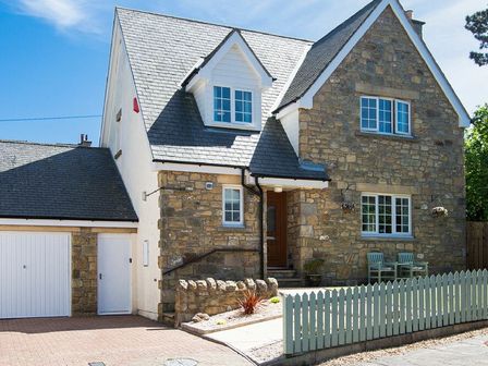 A stone and white exterior house with a garage and a white picket fence at Castlewood in Bamburgh