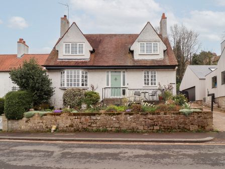 A two story house with a stone wall and garden in front at Rosedale Lodge in Alnmouth