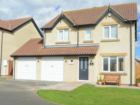 A detached house with two white garage doors a black front door wooden bench and grass at Luna Tide in Seahouses