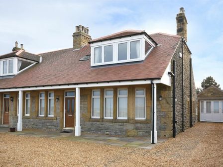 A stone house with a tiled roof multiple windows and two brown doors at Bradacar in Seahouses