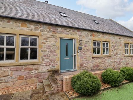 Exterior of a stone building with a blue door and multiple windows with bushes in front at The Old Stables in Bamburgh