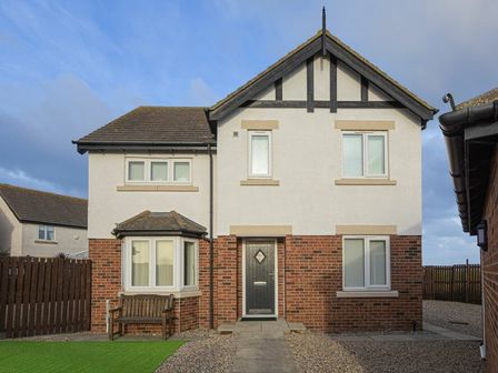 A two story house with brick and white exterior with a wooden bench outside Coastal View in Seahouses