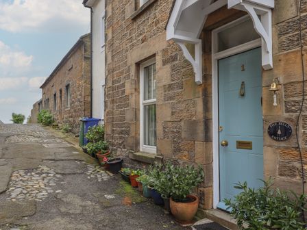 Stone cottages along a cobbled street with blue door and potted plants outside at Five Bells Cottage in Alnmouth