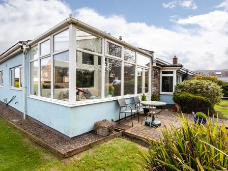 A patio area with a round table and two chairs outside a house with a large window at Palmers Rest in Beadnell