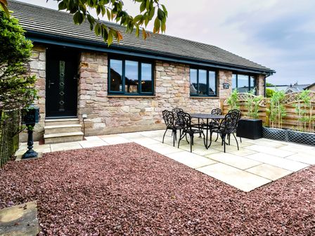 An outdoor patio with a black metal table and six chairs beside a stone house with three windows and a black door at Polished Pebble in Beadnell