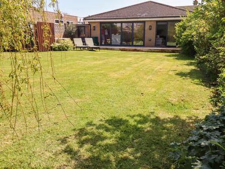 A backyard with a grass lawn loungers and a single-story house with large glass doors and windows at Willow in Beadnell