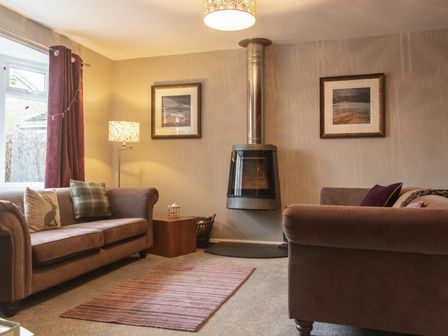 A sitting room with two sofas a wall-mounted fireplace and framed pictures at Our Story Cottage in Longhoughton
