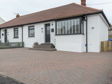 A single-story house with white walls brown roof and paved driveway at Southfield Lodge in Seahouses
