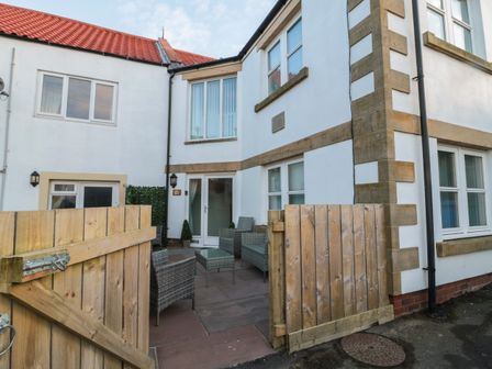 An outdoor patio area with wicker chairs, a glass table, and wooden gate at Butcher's Retreat in Seahouses