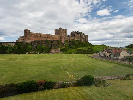 A large castle on a hill with green fields and a few houses nearby at Keepers View in Bamburgh