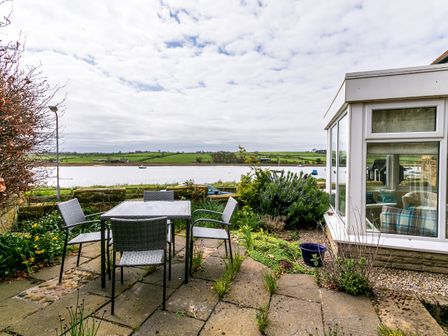 A patio area with a table and four chairs overlooking a river and green fields at The Beach House Alnmouth