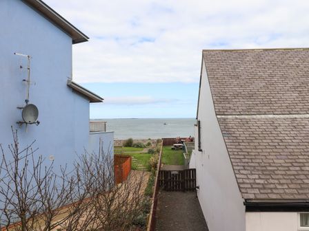 A view of the sea between a blue building and a white building with a tiled roof at Puffin View in Seahouses