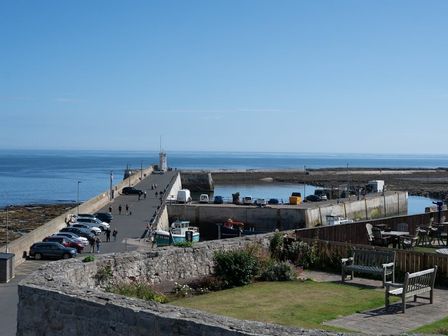 A harbor with parked cars and fishing boats with benches and tables in a grassy area at Keildon in Seahouses