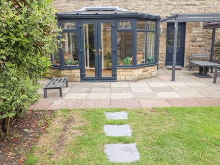 A garden patio area with stone paving a small bench a glass conservatory and a stone building at Muscle Shoals in Seahouses