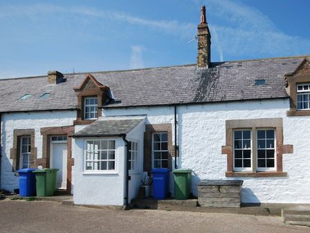 A white stone cottage with multiple windows a small porch and recycling bins outside at Sandpiper Cottage Low Newton-by-the-Sea