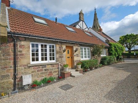 A stone cottage with white framed windows and a wooden door with small steps outside at Grange Cottage in Alnmouth