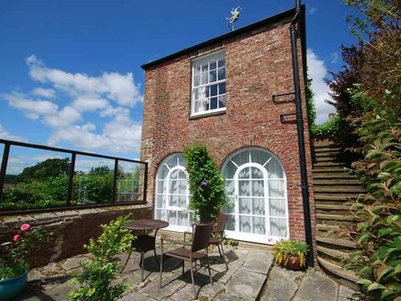 A brick building with white framed arched windows and an outdoor patio with a table and chairs at The Old Watchtower in Alnmouth