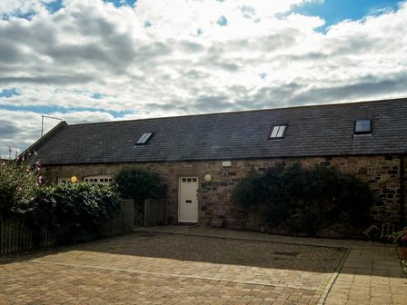 A stone building with a pitched roof skylights a white door bushes and a paved courtyard at High Tide in Newton-by-the-Sea