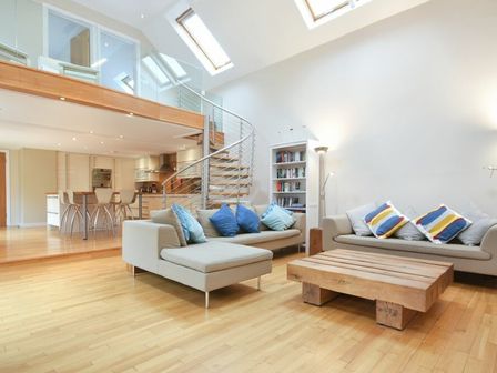 A living room with beige sofas with cushions a wooden coffee table a bookshelf and spiral stairs at Links Barn in Seahouses