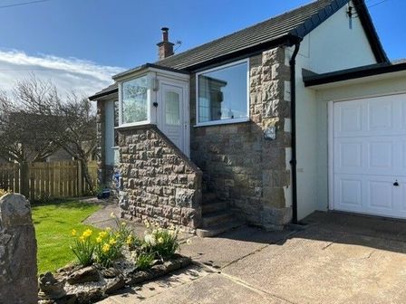 Exterior of a stone and brick house with steps leading to a white door and a driveway with a garage at Sea Croft in Beadnell