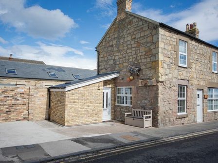 A stone house with a bench outside on a sidewalk at Lobster Pot Cottage in Seahouses