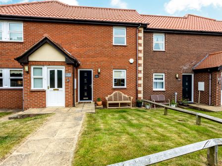 The front exterior of brick townhouses with a tiled roof a paved pathway green lawn wooden and metal benches and potted plants at The Apartment in Bamburgh