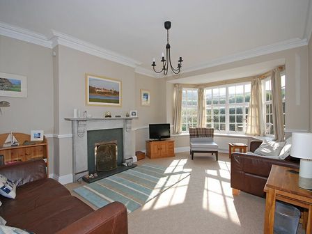A living room with leather sofas a fireplace a chandelier and a bay window at Beach House Alnmouth